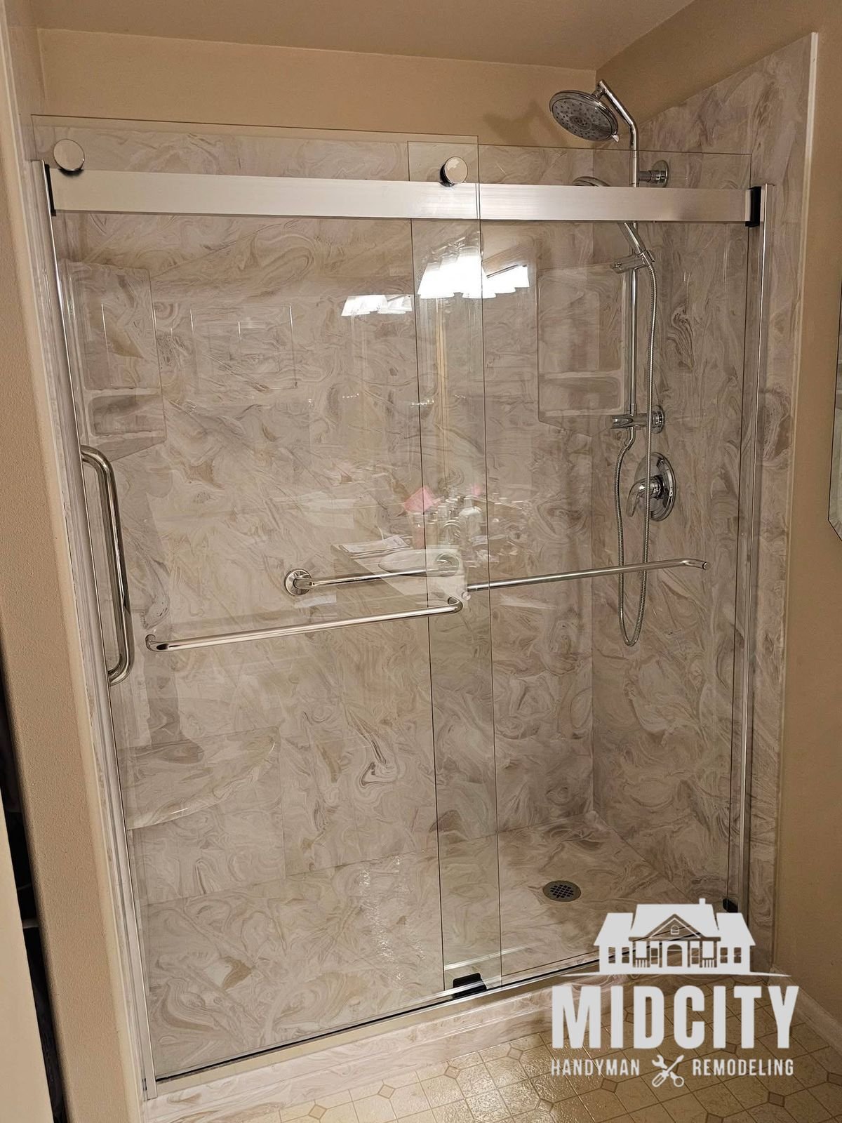 Walk-in shower with marble look tile and sliding glass door by Midcity Handyman & Remodeling
